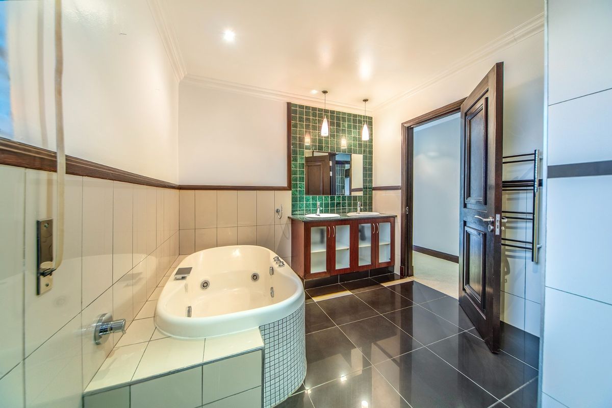 Spacious bathroom featuring a built-in spa bath, double vanity with green tiled splashback, dark floor tiles, and a heated towel rail.