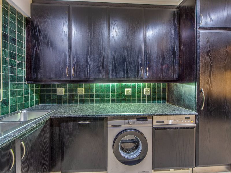 A functional kitchen featuring dark wood cabinetry, granite countertops, a green tiled backsplash, and integrated laundry and dishwashing appliances.