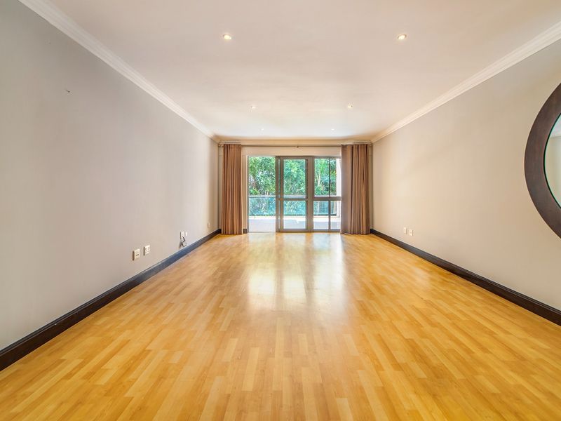A spacious, empty living room featuring light laminate flooring, recessed downlighting, and a large sliding glass door providing access to the balcony.