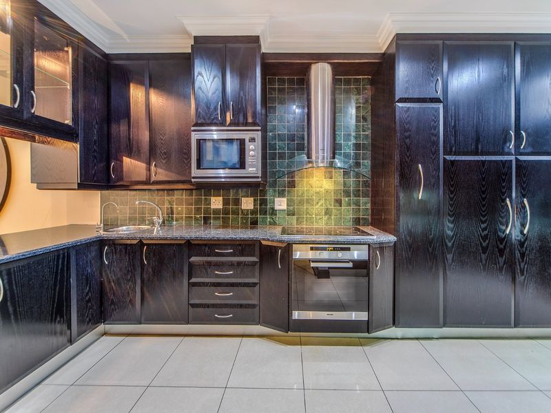 Modern kitchen featuring dark wood cabinetry, granite countertops, integrated stainless steel appliances, and a tiled backsplash.