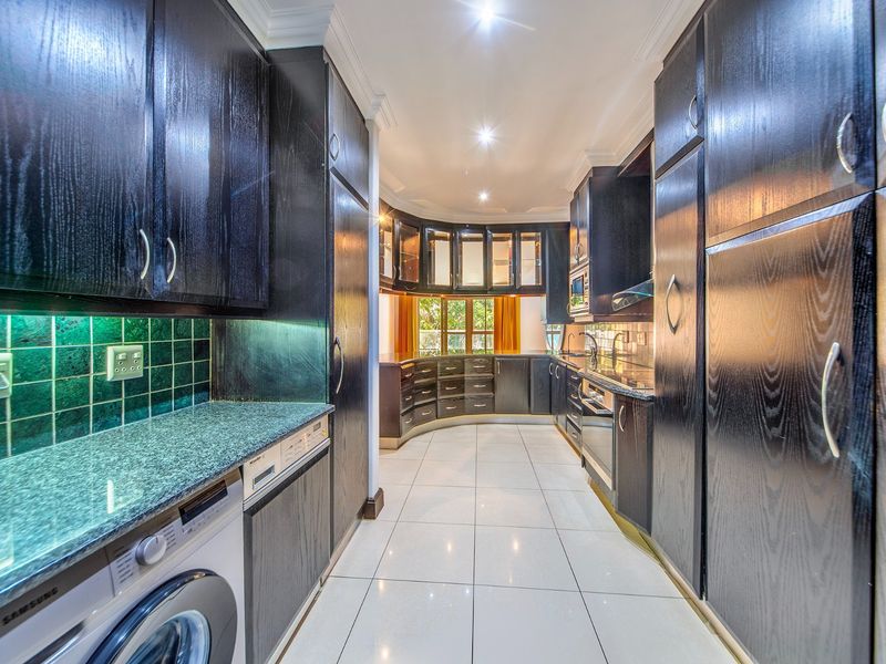 A well-appointed kitchen featuring dark wood cabinetry, granite countertops, integrated appliances, and tiled flooring, offering a functional and stylish culinary space.