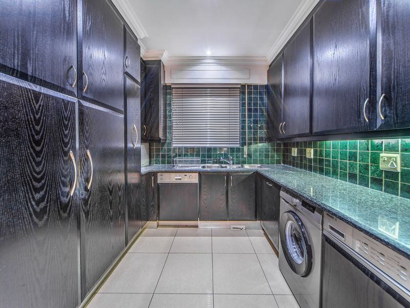 A well-appointed kitchen featuring dark wood cabinetry, granite countertops, tiled backsplash, and integrated appliances including a dishwasher and washing machine.