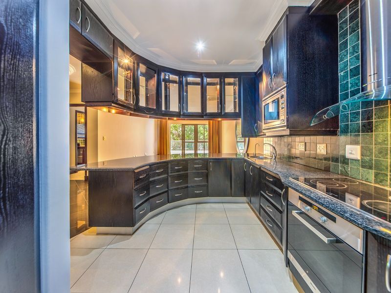 A modern kitchen featuring dark wood curved cabinetry, granite countertops, integrated appliances, and a tiled backsplash with under-cabinet lighting.
