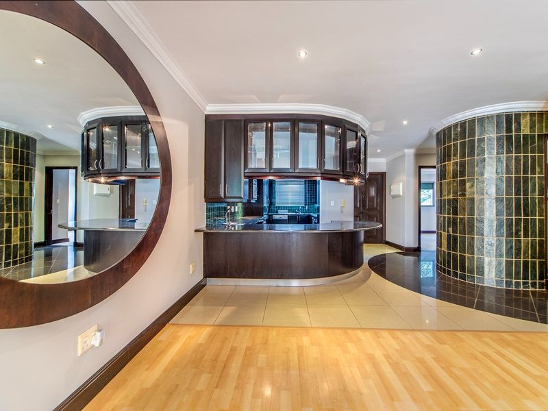A modern kitchen area featuring dark wood cabinetry, a curved breakfast bar, and unique tiled feature wall, offering a functional and stylish layout.