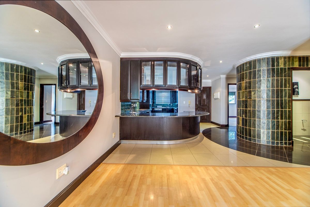A modern kitchen area featuring dark wood cabinetry, a curved breakfast bar, and unique tiled feature wall, offering a functional and stylish layout.