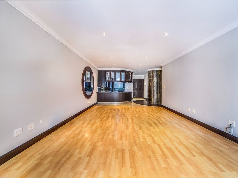 Spacious open-plan living area featuring laminate flooring, recessed lighting, and a built-in kitchen counter with dark cabinetry.
