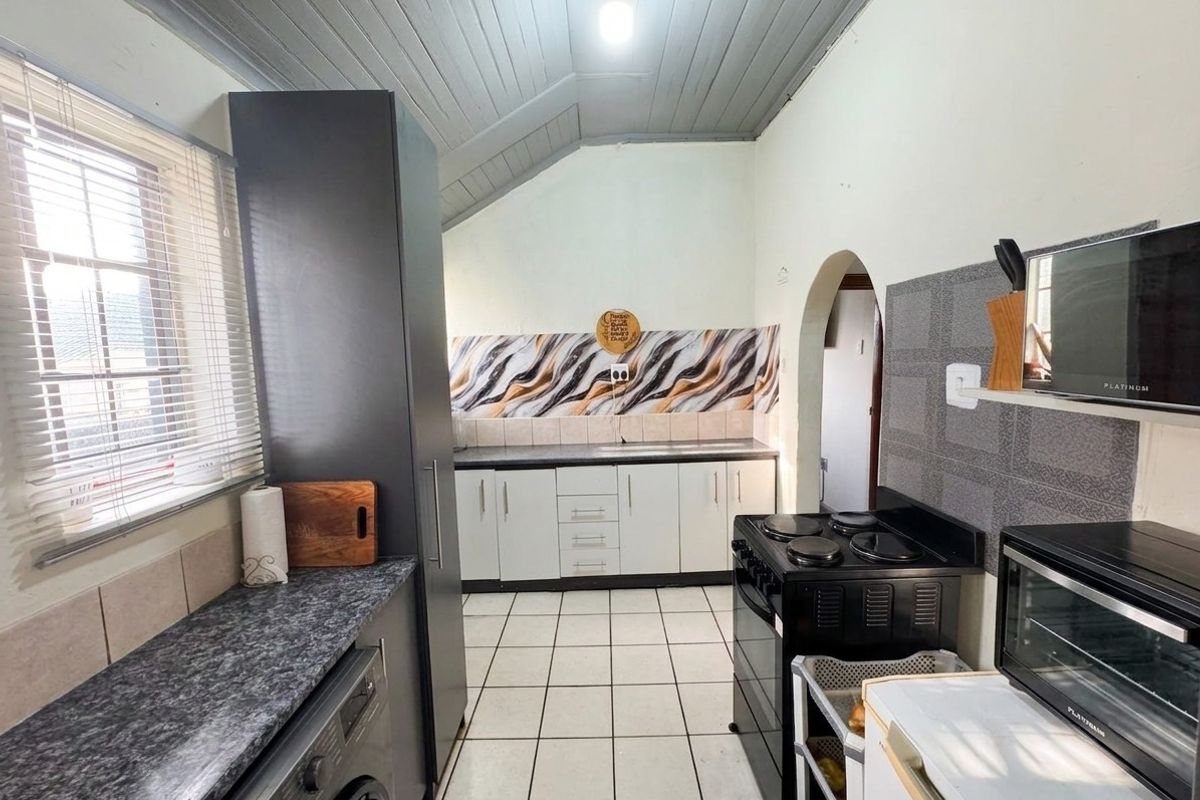 A functional kitchen featuring tiled flooring, laminate countertops, built-in cabinetry, and a distinctive timber panelled ceiling with an arched doorway.