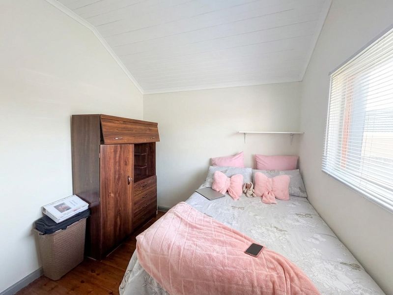 A compact bedroom featuring timber flooring, a white tongue and groove ceiling, and a window fitted with venetian blinds.