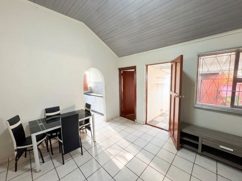 Open plan living and dining area featuring vaulted ceilings, tiled flooring, and an arched entryway leading to the kitchen.