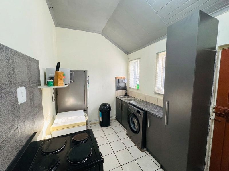 Functional laundry room featuring built-in cabinetry, laminate countertops, a stainless steel sink, and tiled flooring with a sloped ceiling.