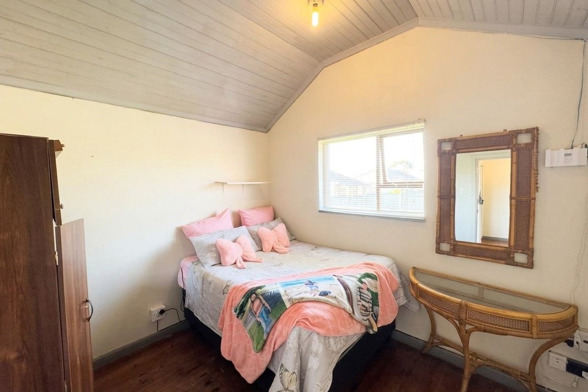 A cozy bedroom featuring timber flooring and a vaulted timber ceiling, providing a warm and rustic atmosphere with natural light from the sliding window.