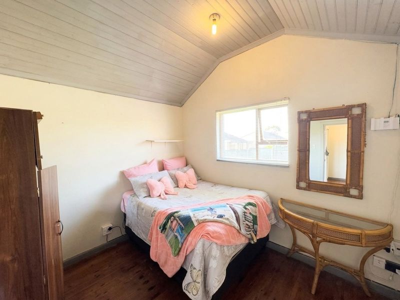 A cozy bedroom featuring timber flooring and a vaulted timber ceiling, providing a warm and rustic atmosphere with natural light from the sliding window.