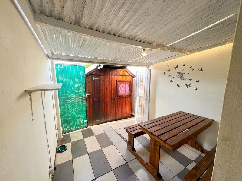 A covered outdoor patio area featuring tiled flooring, a corrugated metal roof, and a built-in wooden storage shed.