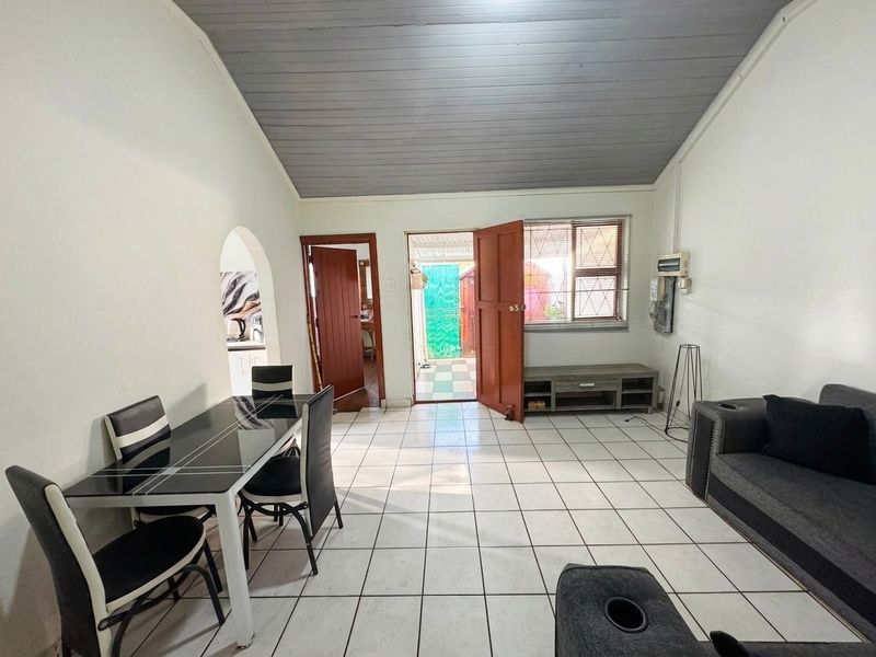 Open-plan living and dining area featuring tiled flooring, a vaulted timber ceiling, and direct access to the exterior through a security door.