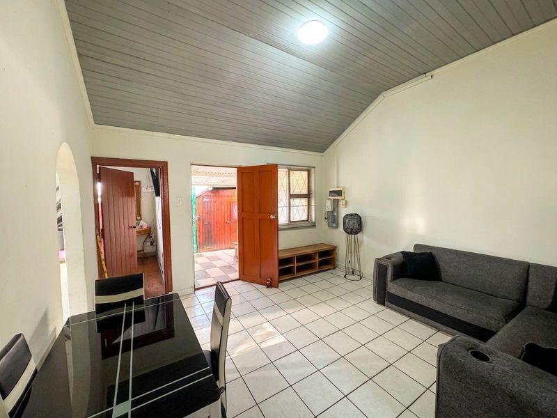 Open plan living area featuring tiled flooring, a vaulted ceiling, and direct access to an outdoor space through a timber door.