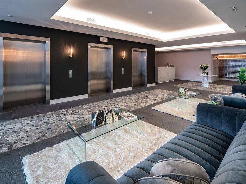 Modern building lobby featuring stainless steel elevator banks, recessed ceiling lighting, stone flooring, and a dedicated reception area with integrated mailboxes.