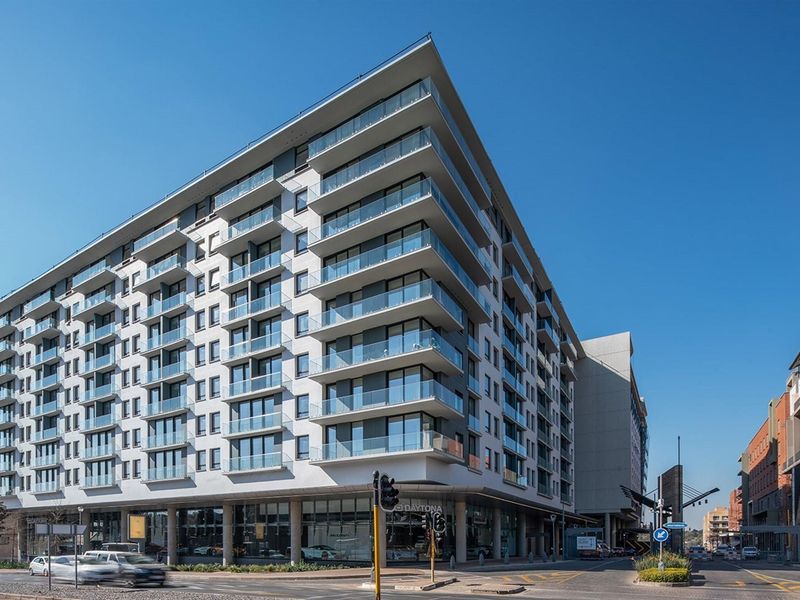 Modern multi-story residential building featuring a prominent corner facade with extensive glass balustrades and a commercial ground floor level.