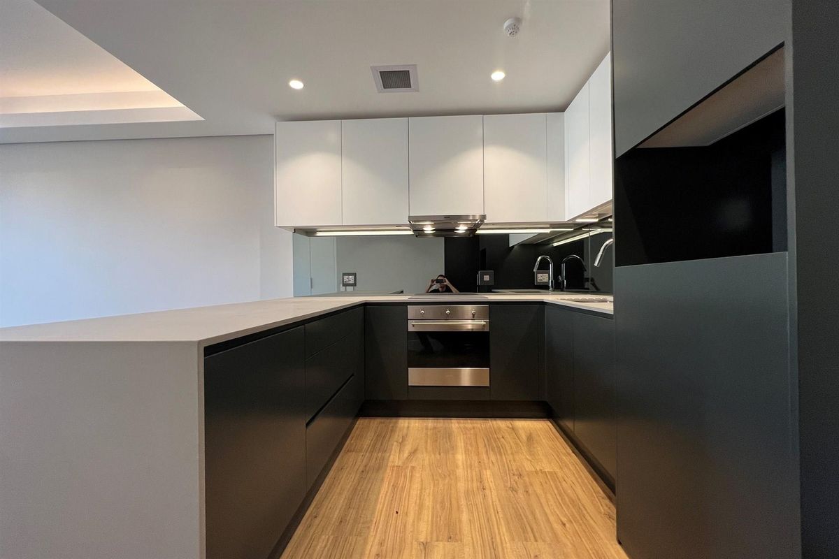 Modern kitchen featuring sleek handleless cabinetry, stone benchtops, a mirrored splashback, and integrated stainless steel appliances in a clean, minimalist design.