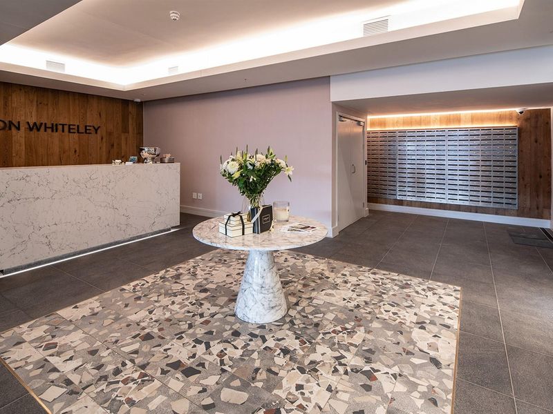 Modern building entrance lobby featuring a stone reception desk, integrated mailboxes, recessed lighting, and a combination of terrazzo and tile flooring.