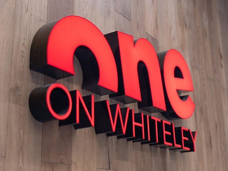 A close-up view of a modern illuminated building sign mounted on a wood-look paneled wall.