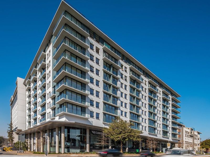 A modern multi-story residential building featuring glass balconies, large windows, and a prominent ground-floor commercial space.