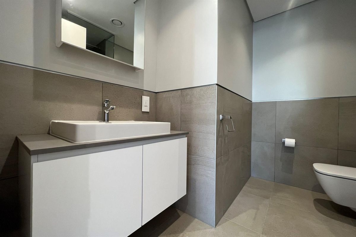 Modern bathroom featuring a wall-mounted vanity with a ceramic basin, wall-hung toilet, and neutral large-format tiling throughout.