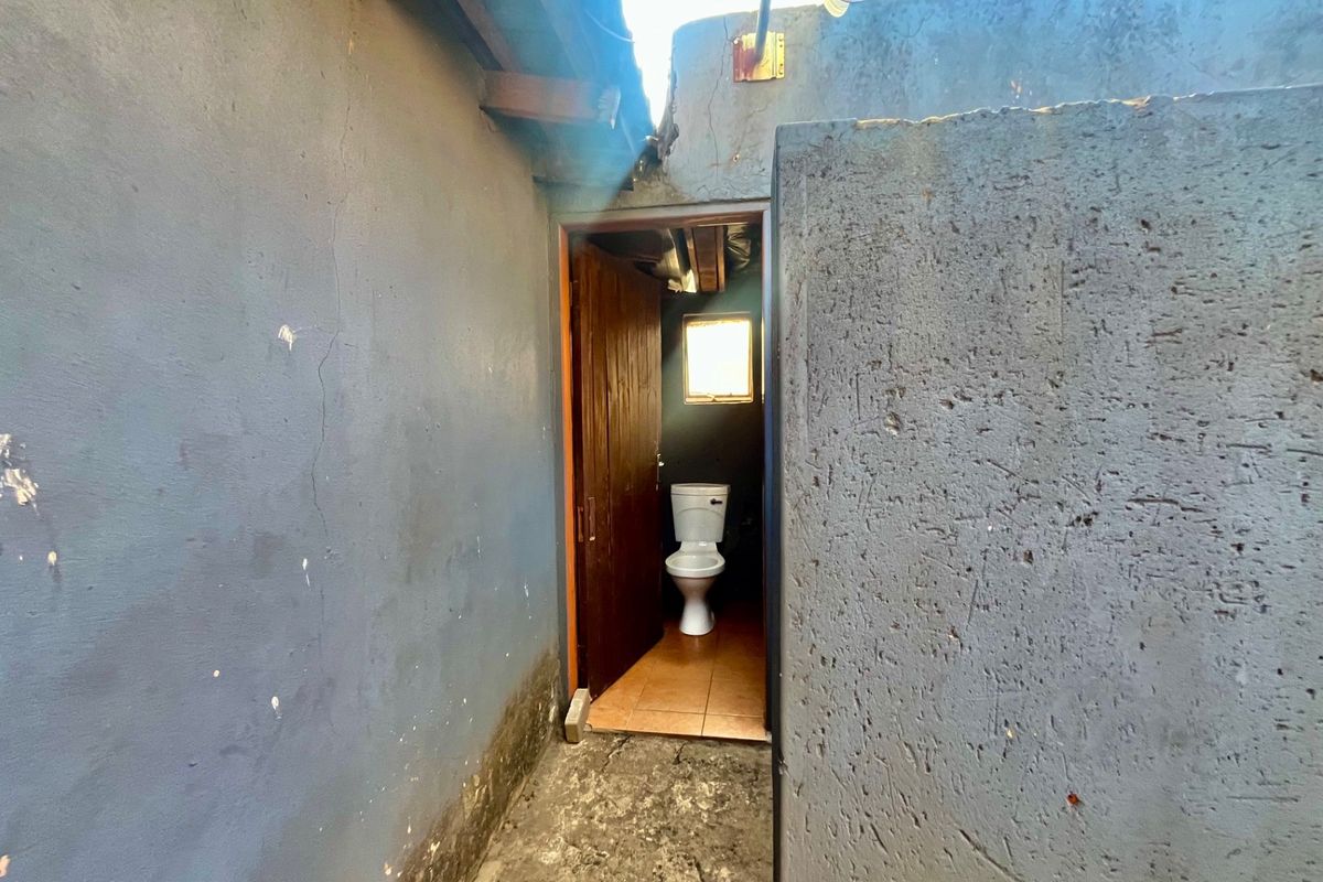 A small, basic bathroom featuring a toilet and tiled flooring, requiring significant maintenance and cosmetic updates to the surrounding exterior and interior wall finishes.