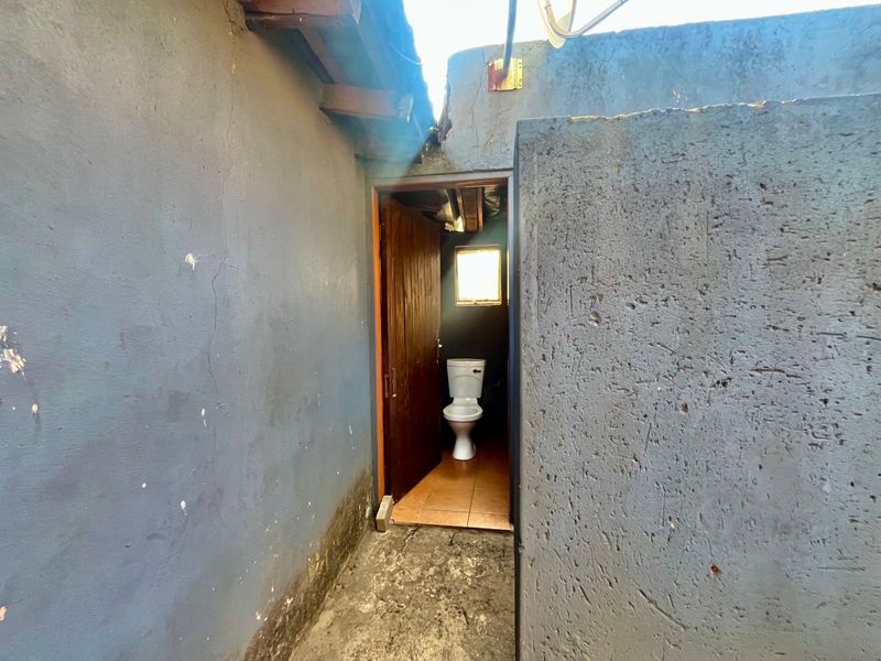A small, basic bathroom featuring a toilet and tiled flooring, requiring significant maintenance and cosmetic updates to the surrounding exterior and interior wall finishes.