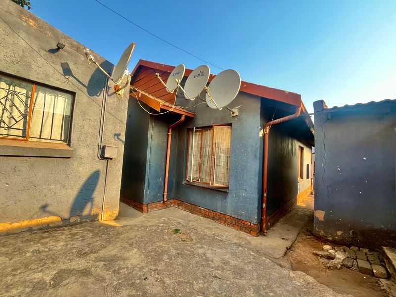Rear exterior view of the property featuring multiple satellite dishes, metal window frames, and concrete paving with visible signs of wear and exterior maintenance needs.