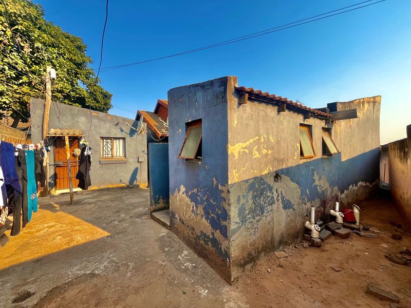 Rear exterior view of the property showing a paved courtyard area and outbuilding with visible wear to the exterior wall finishes.