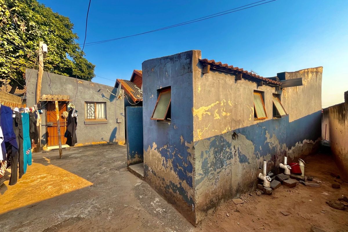 Rear exterior view of the property showing a paved courtyard area and outbuilding with visible wear to the exterior wall finishes.