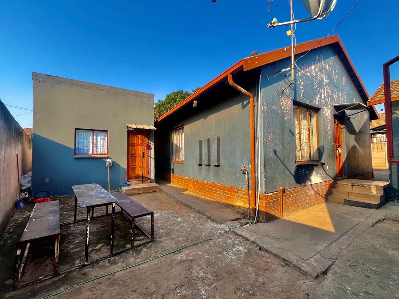 Rear view of the property showing a detached structure, concrete courtyard area, and exterior walls requiring maintenance and repainting.