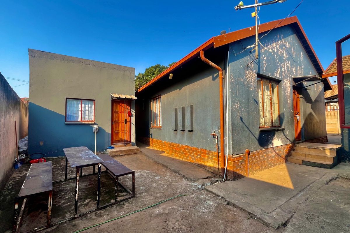 Rear view of the property showing a detached structure, concrete courtyard area, and exterior walls requiring maintenance and repainting.