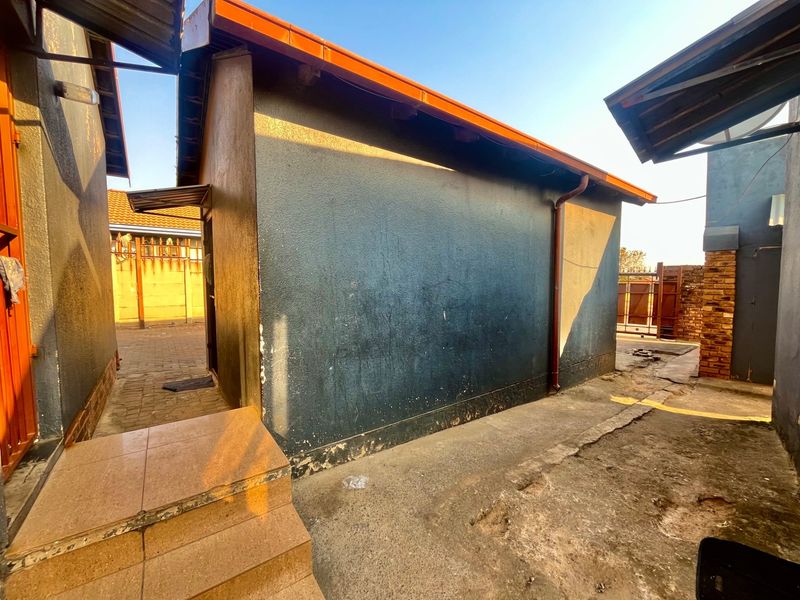 Rear exterior view of the property showing a paved walkway, tiled steps, and painted exterior walls with visible signs of wear.