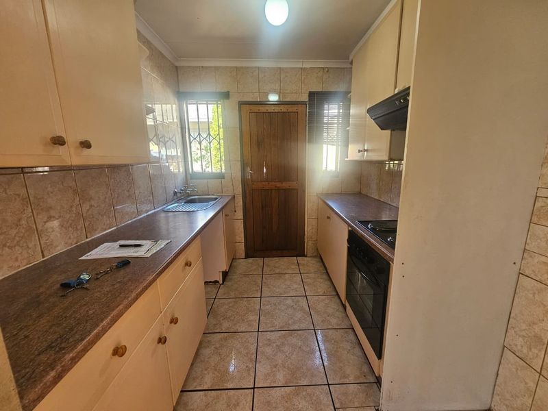 A functional galley-style kitchen featuring built-in cabinetry, laminate countertops, an integrated oven and hob, and tiled finishes throughout.