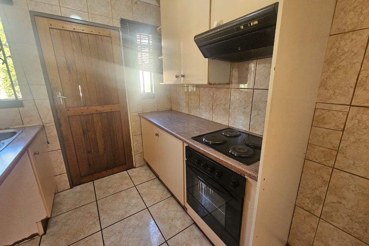 A compact kitchen featuring built-in cabinetry, an electric hob with extractor fan, and tiled surfaces throughout, offering a functional layout with potential for modernization.