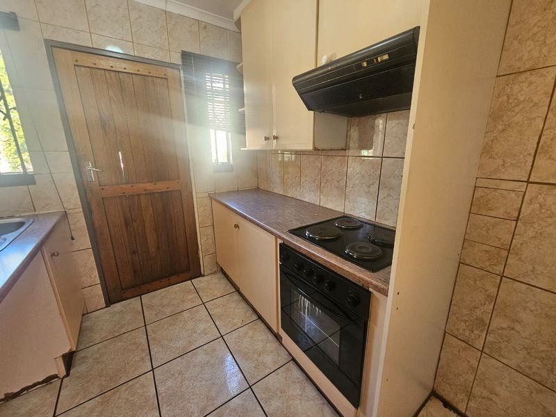 A compact kitchen featuring built-in cabinetry, an electric hob with extractor fan, and tiled surfaces throughout, offering a functional layout with potential for modernization.