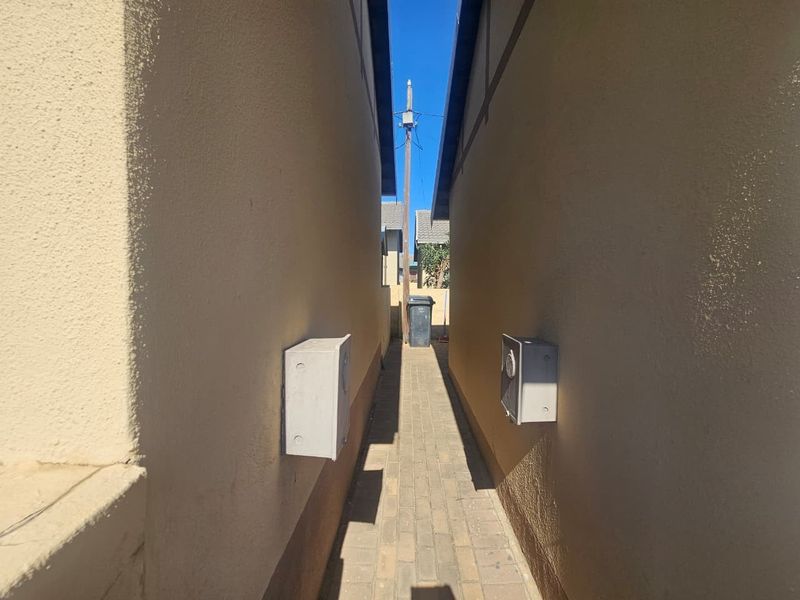 A narrow paved side passage between two townhouse structures featuring exterior electrical meter boxes mounted on the plastered walls.
