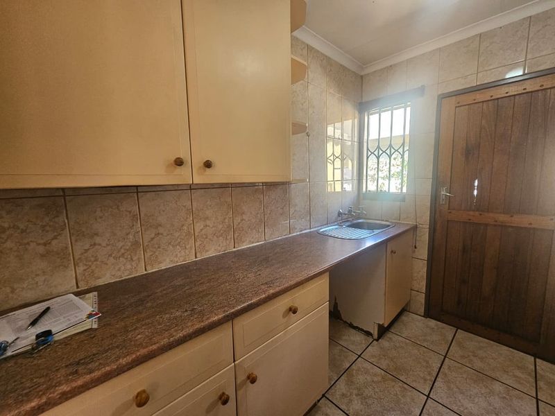 A functional scullery area featuring built-in cabinetry, laminate countertops, a stainless steel sink, and tiled finishes, requiring minor repairs to the base cabinetry.