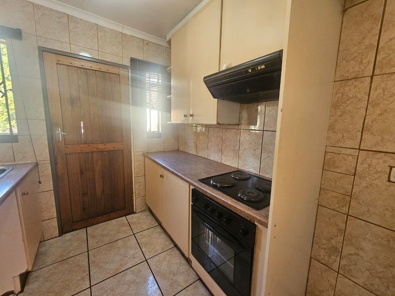 A functional kitchen featuring built-in cabinetry, an electric hob with extractor fan, tiled backsplash, and direct access to an exterior door.