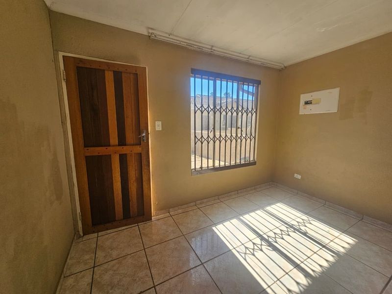 An empty bedroom featuring tiled flooring, a timber door, and a window fitted with a security gate.