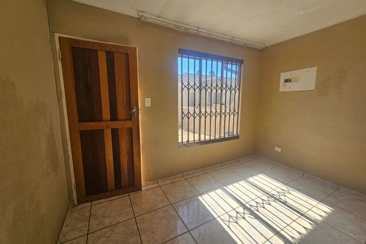 An empty bedroom featuring tiled flooring, a timber door, and a window fitted with a security gate.