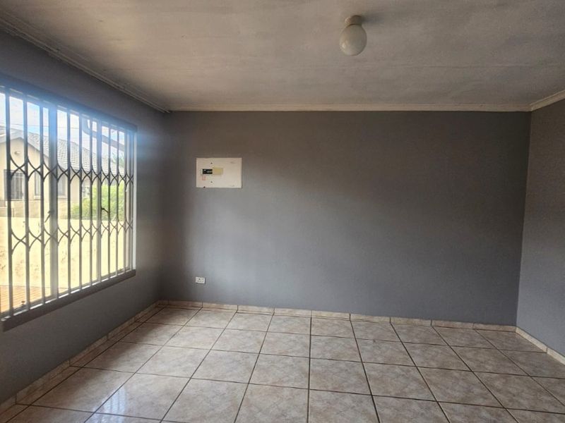 An empty living room featuring neutral tiled flooring, grey walls, and security bars on the window, providing a blank canvas for personalization.