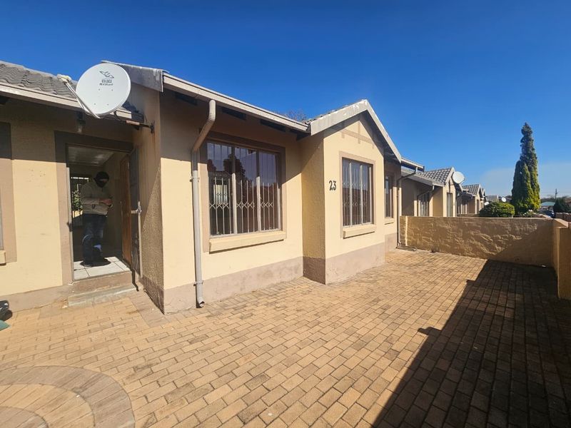 Front exterior view of a townhouse featuring a paved driveway, security bars on windows, and a tiled roof.