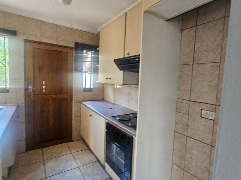 A compact, dated kitchen featuring tiled flooring, built-in cabinetry, an integrated oven and hob, and a solid wood exterior door.
