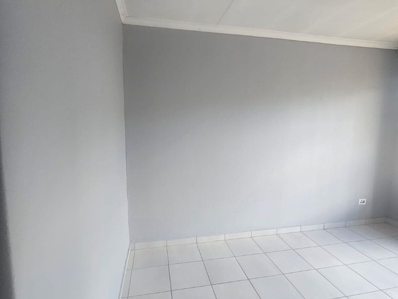 A clean, empty bedroom featuring neutral grey walls, white tiled flooring, and a tiled ceiling.