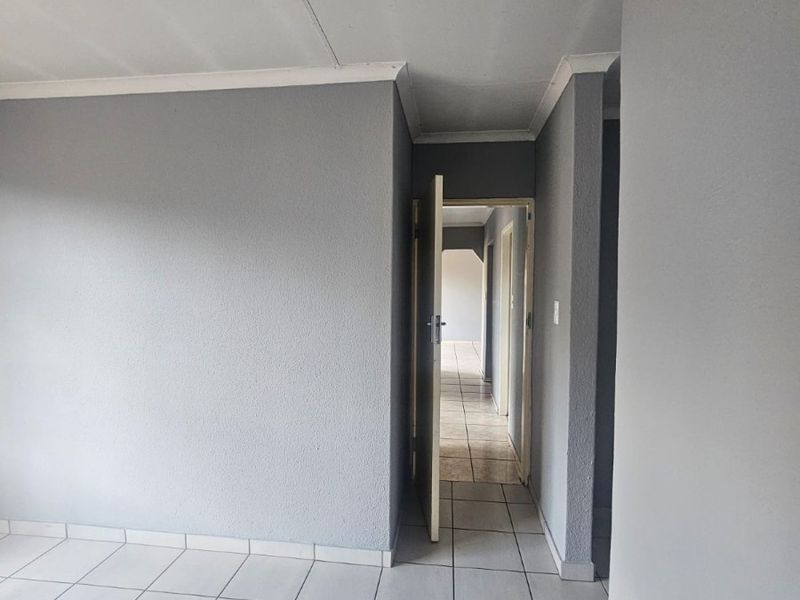 An empty hallway featuring neutral grey walls and tiled flooring, leading to an adjacent room through an open doorway.