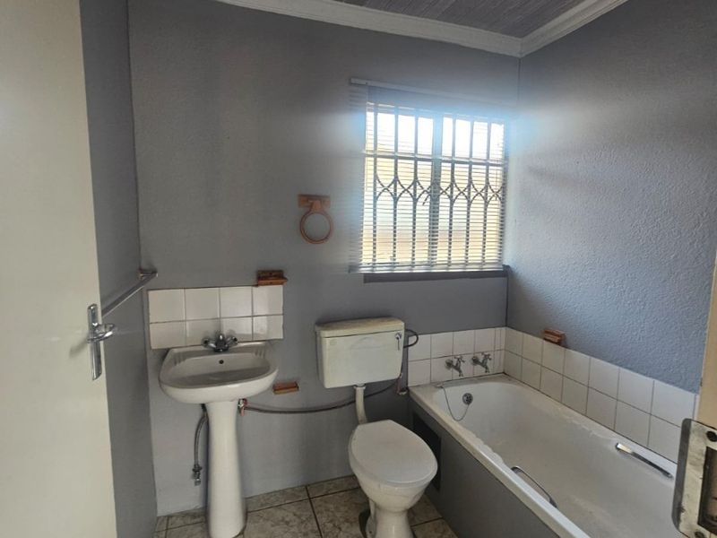 A functional bathroom featuring a pedestal basin, toilet, and bathtub with tiled flooring and security bars on the window.