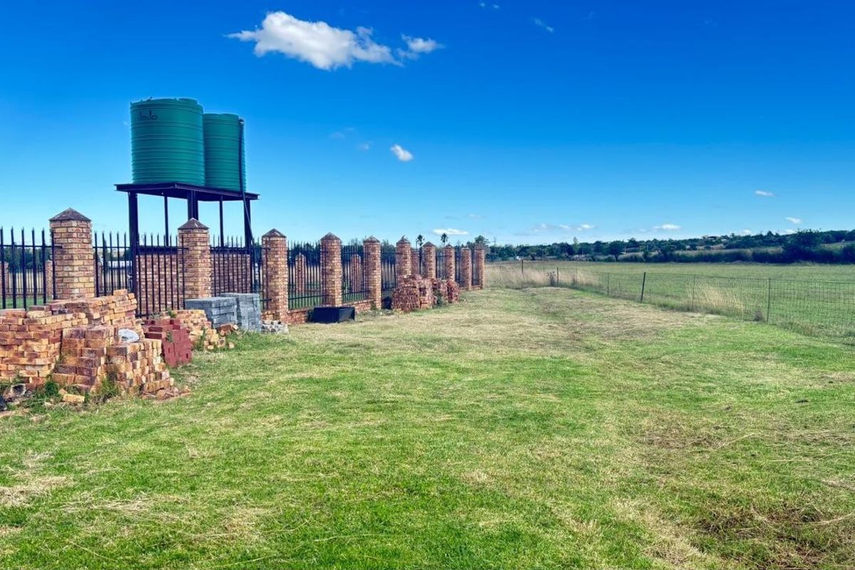 Expansive rear garden area featuring a brick and palisade perimeter wall, elevated water storage tanks on a steel stand, and open field views.