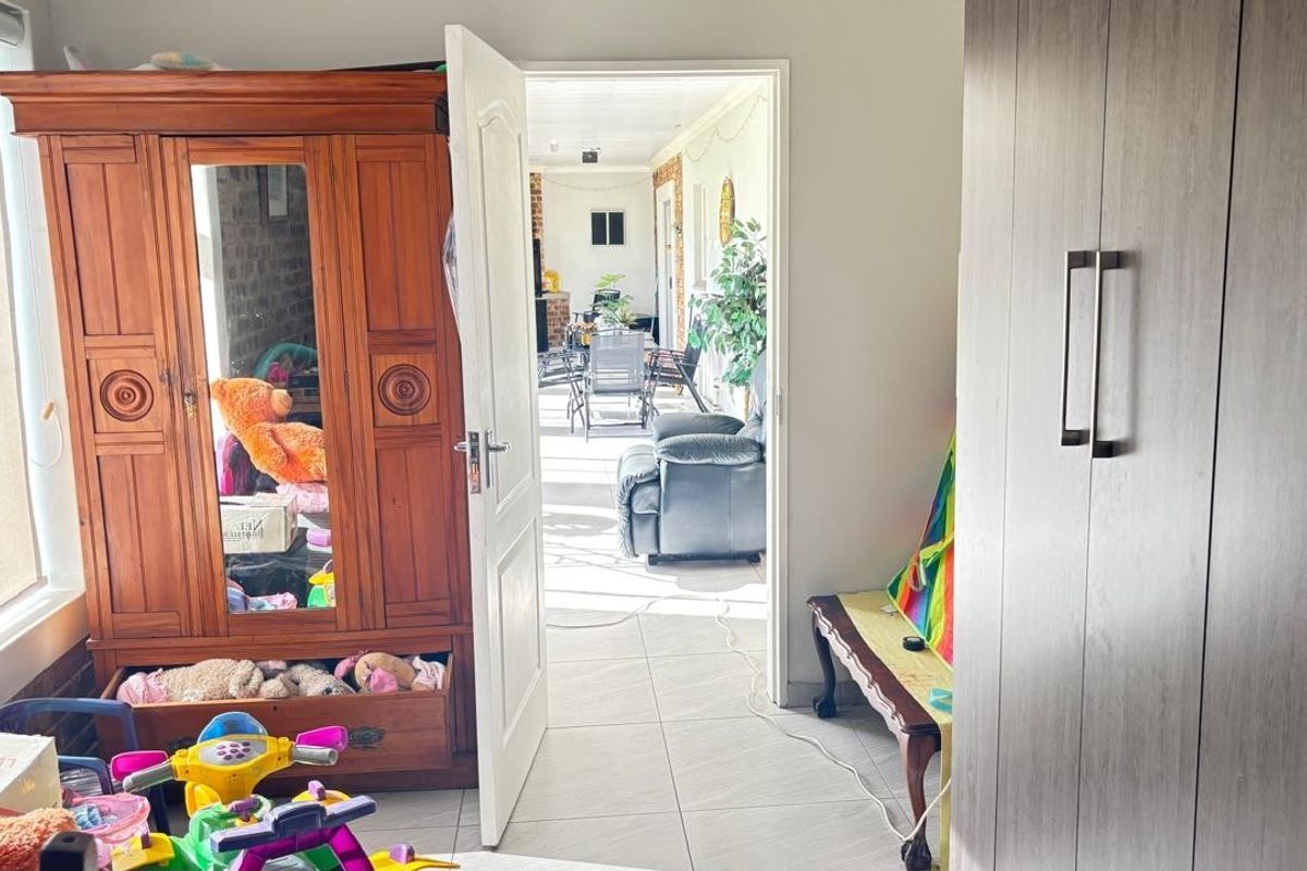 A bedroom featuring tiled flooring and built-in cupboards, with a doorway leading through to an adjacent living area.